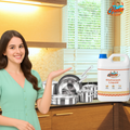 Smiling woman standing in kitchen with GleamSure Dishwash Liquid near sink full of utensils.
